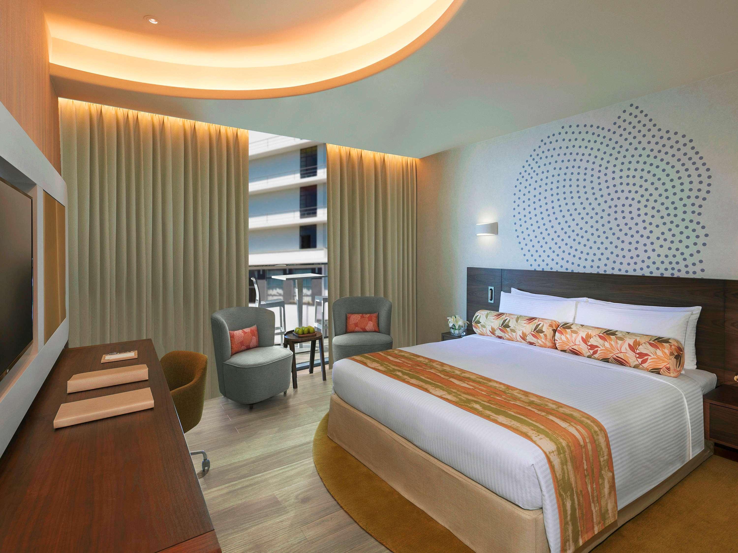 The Retreat Palm Dubai Mgallery By Sofitel Esterno foto The photo shows a modern hotel room featuring a spacious and inviting layout. There is a large bed with decorative pillows, complemented by a colorful bedspread. On either side of the bed, there are two stylish chairs with small tables. The room is w