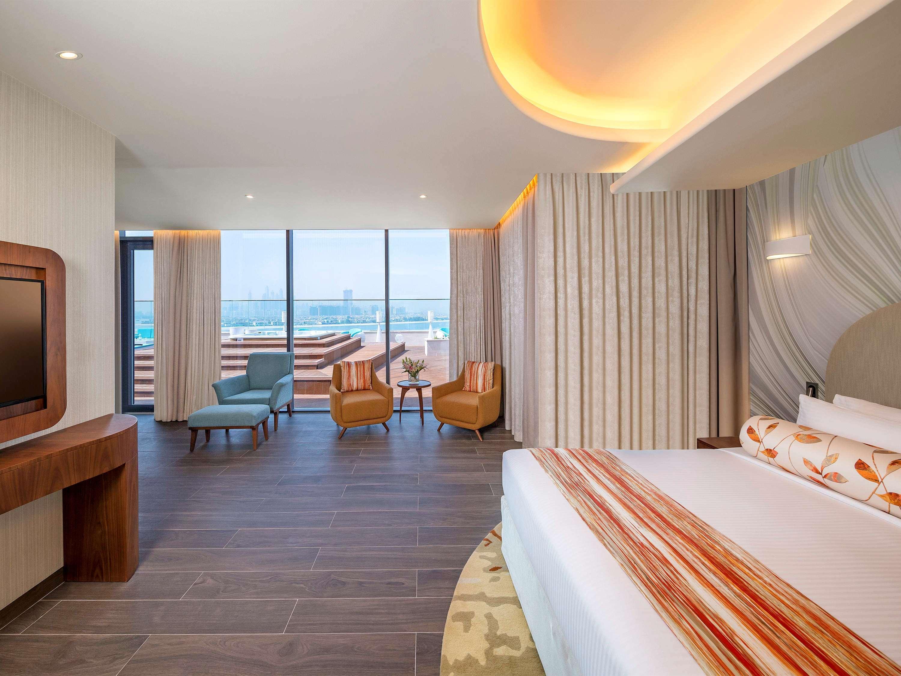 The Retreat Palm Dubai Mgallery By Sofitel Esterno foto The photo shows a modern hotel room featuring a large bed with decorative pillows and a stylish bedspread. The space is bright and airy, illuminated by natural light coming in through large windows that offer a view of the outdoors. There are two com