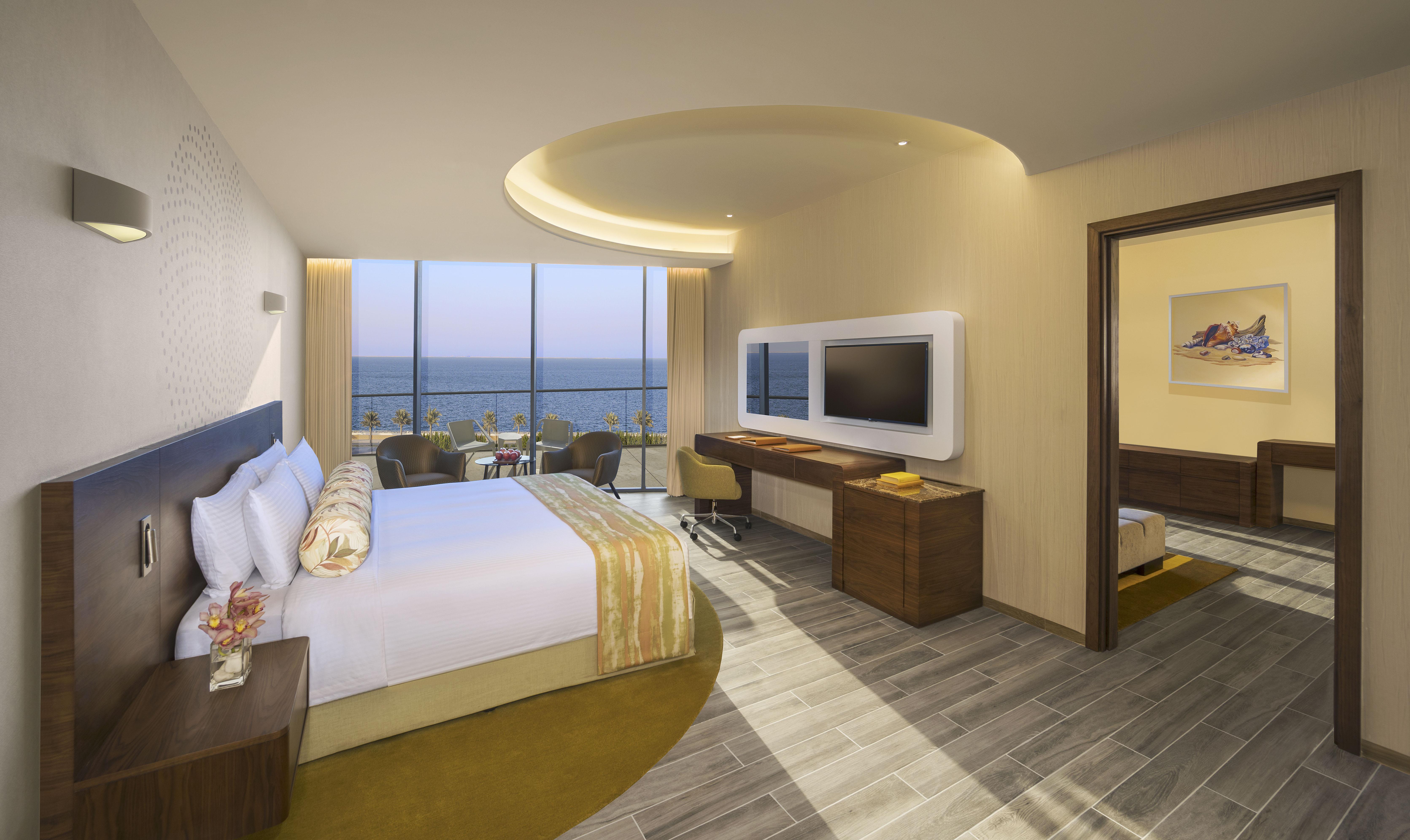 The Retreat Palm Dubai Mgallery By Sofitel Esterno foto The photo depicts a modern hotel room featuring a large bed with white and yellow bedding. The room is well-lit with natural light coming through large glass windows that offer a view of the ocean. There is a comfortable seating area and a flat-scree