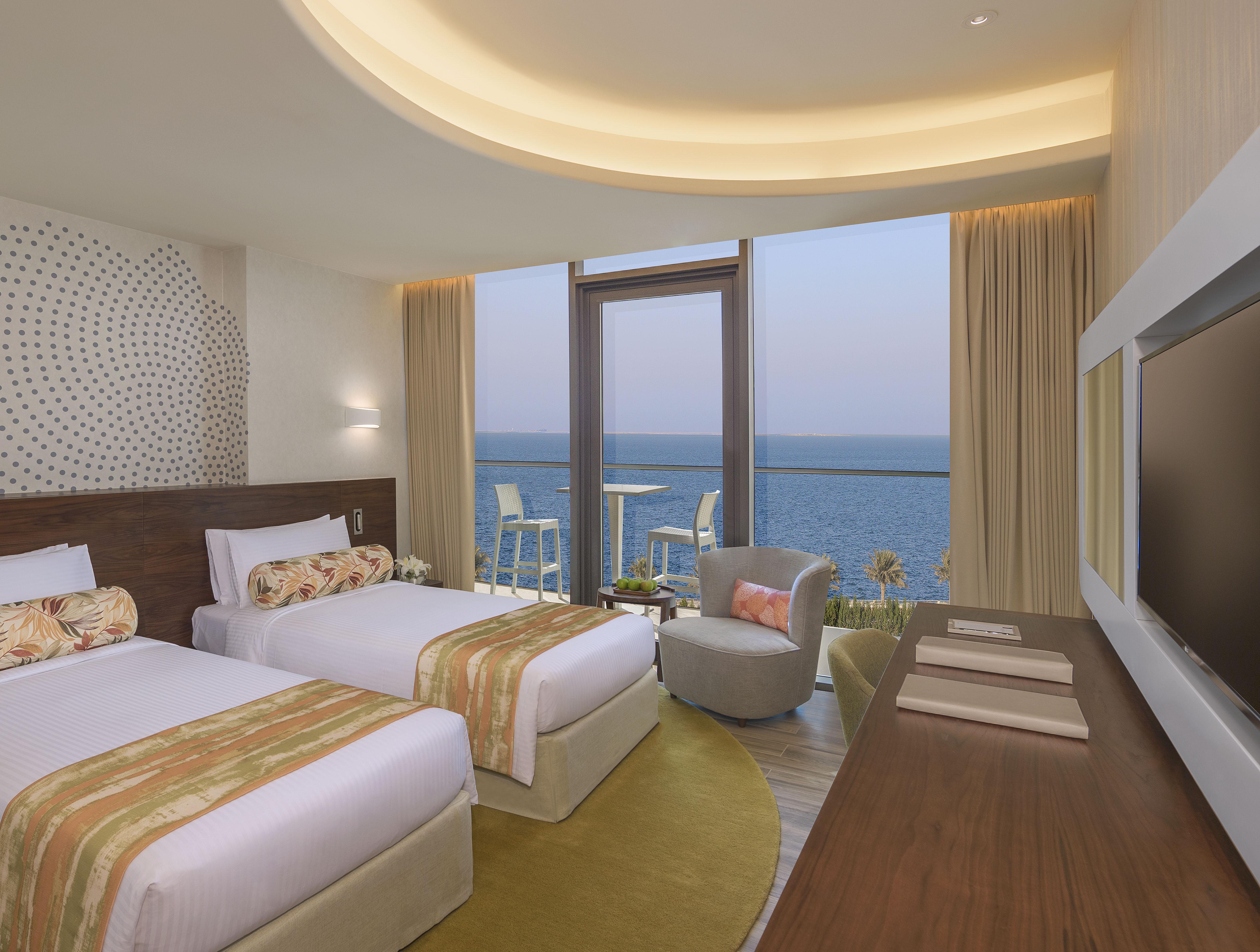 The Retreat Palm Dubai Mgallery By Sofitel Esterno foto The photo shows a modern hotel room with two twin beds, each adorned with decorative pillows and bed runners. The room has large windows that provide a scenic view of the ocean, allowing natural light to fill the space. There is a comfortable armchai