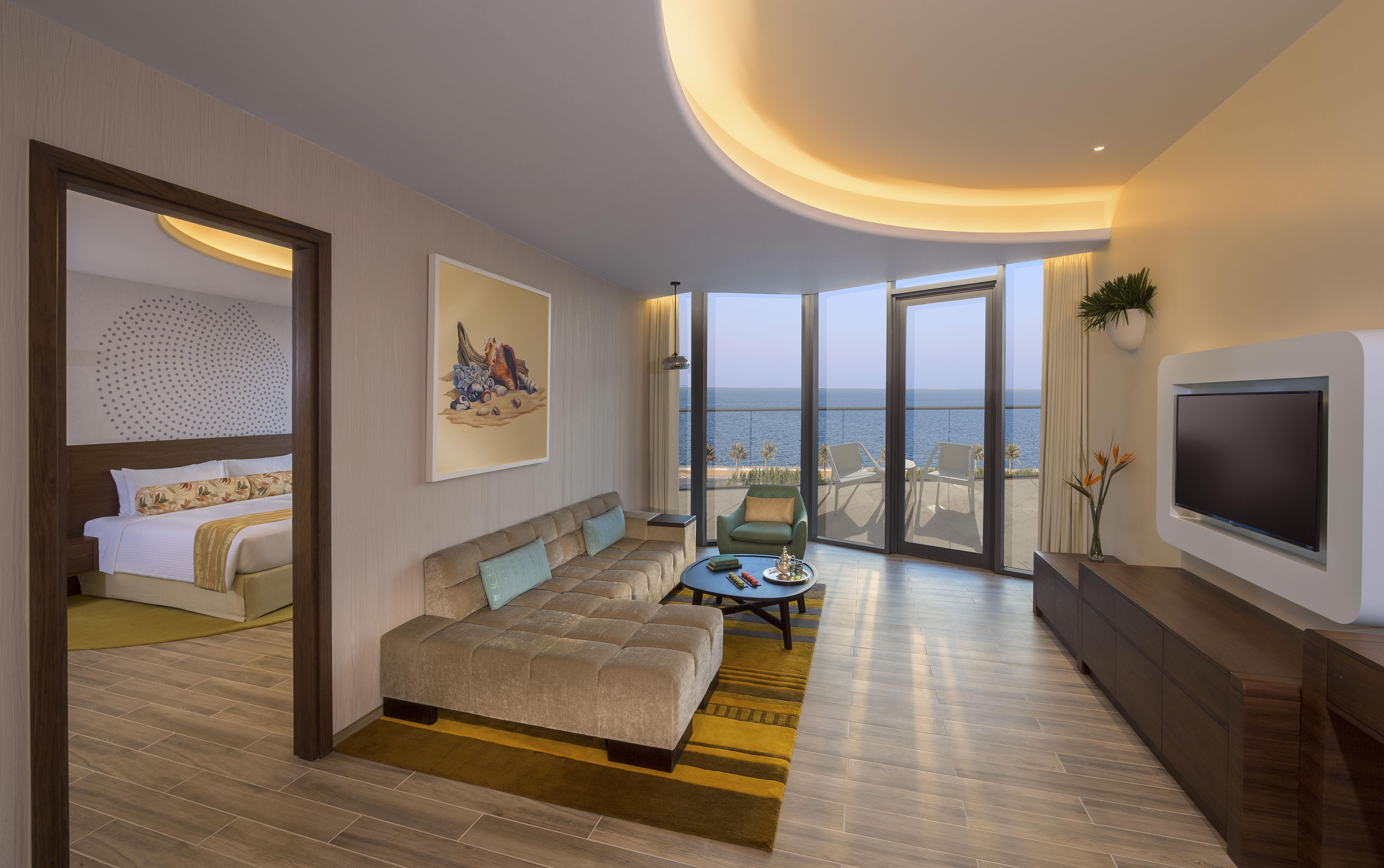 The Retreat Palm Dubai Mgallery By Sofitel Esterno foto The photo shows a modern and stylish hotel suite or living area. It features a comfortable, light-colored sectional sofa with blue cushions, positioned on a wooden floor. There's a coffee table on a patterned area rug in front of the sofa. The walls 