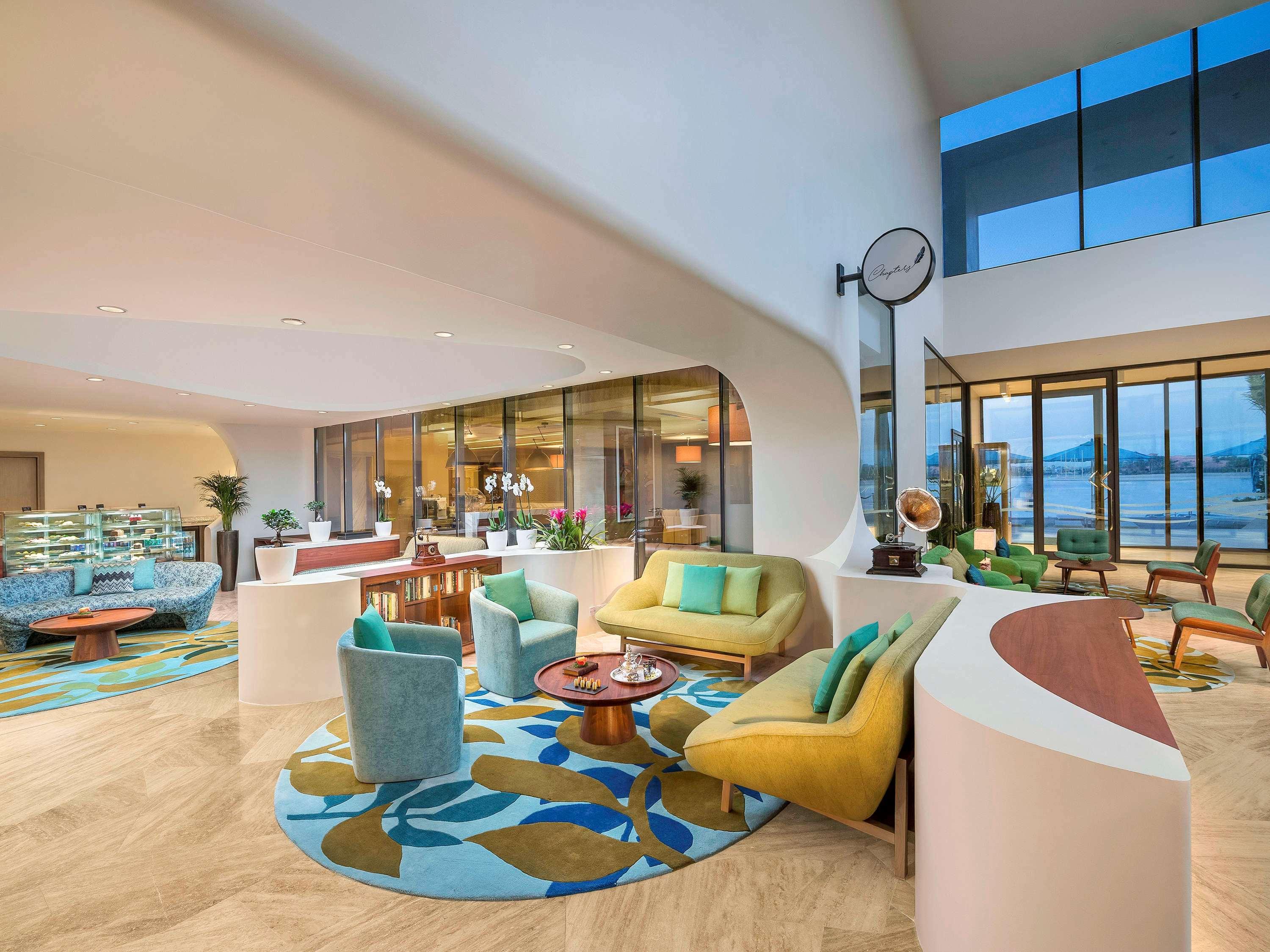 The Retreat Palm Dubai Mgallery By Sofitel Esterno foto The photo shows a stylish and modern interior space, likely a lobby or lounge area. It features a variety of seating arrangements with colorful furniture, including chairs and sofas in shades of blue and yellow. There is a large round rug with a flor