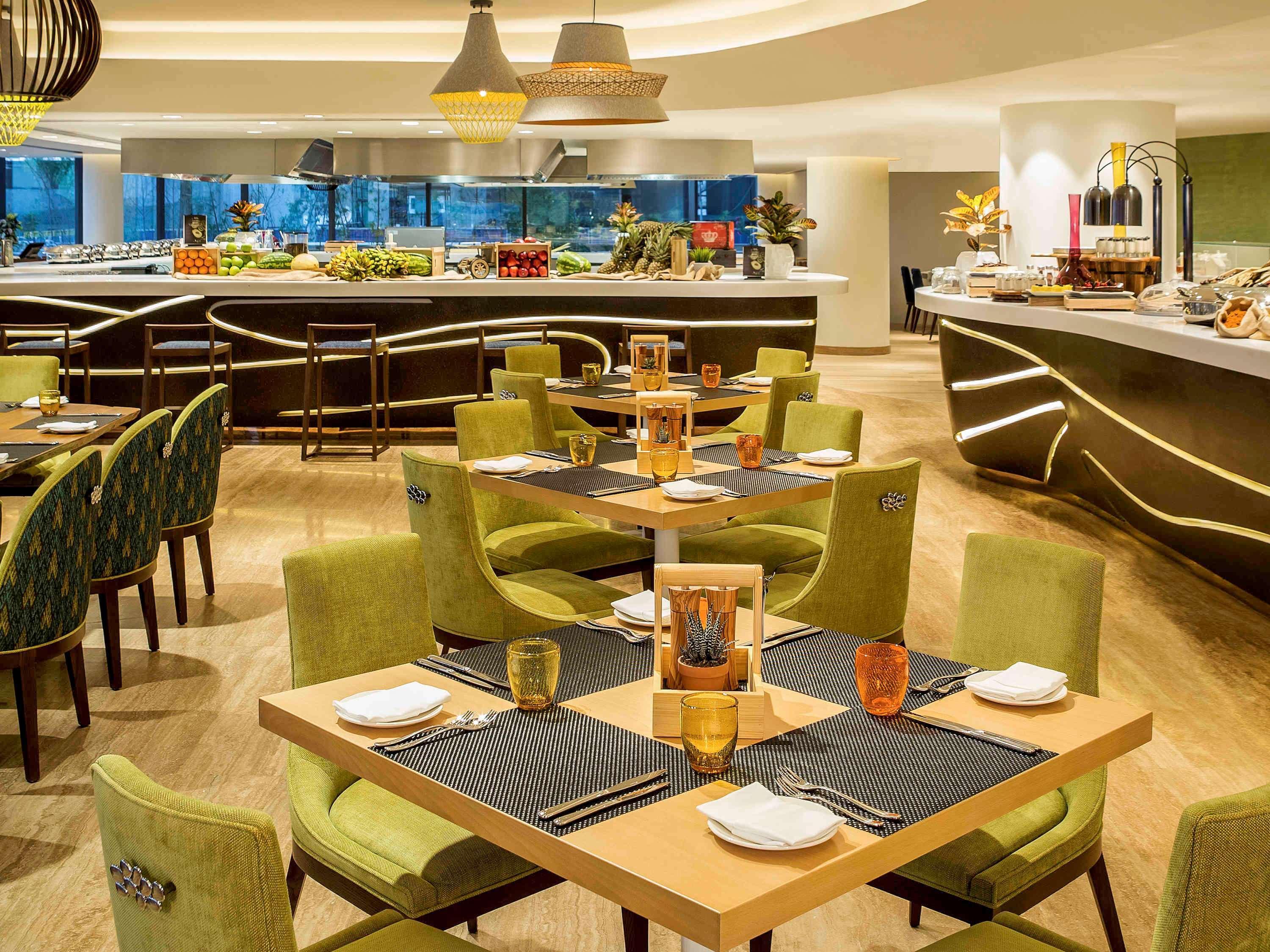 The Retreat Palm Dubai Mgallery By Sofitel Esterno foto The photo shows a modern restaurant interior featuring a spacious dining area. The tables are arranged with green upholstered chairs and are set with plates, cutlery, and glasses. The tables are topped with dark placemats and a small wooden centerpie