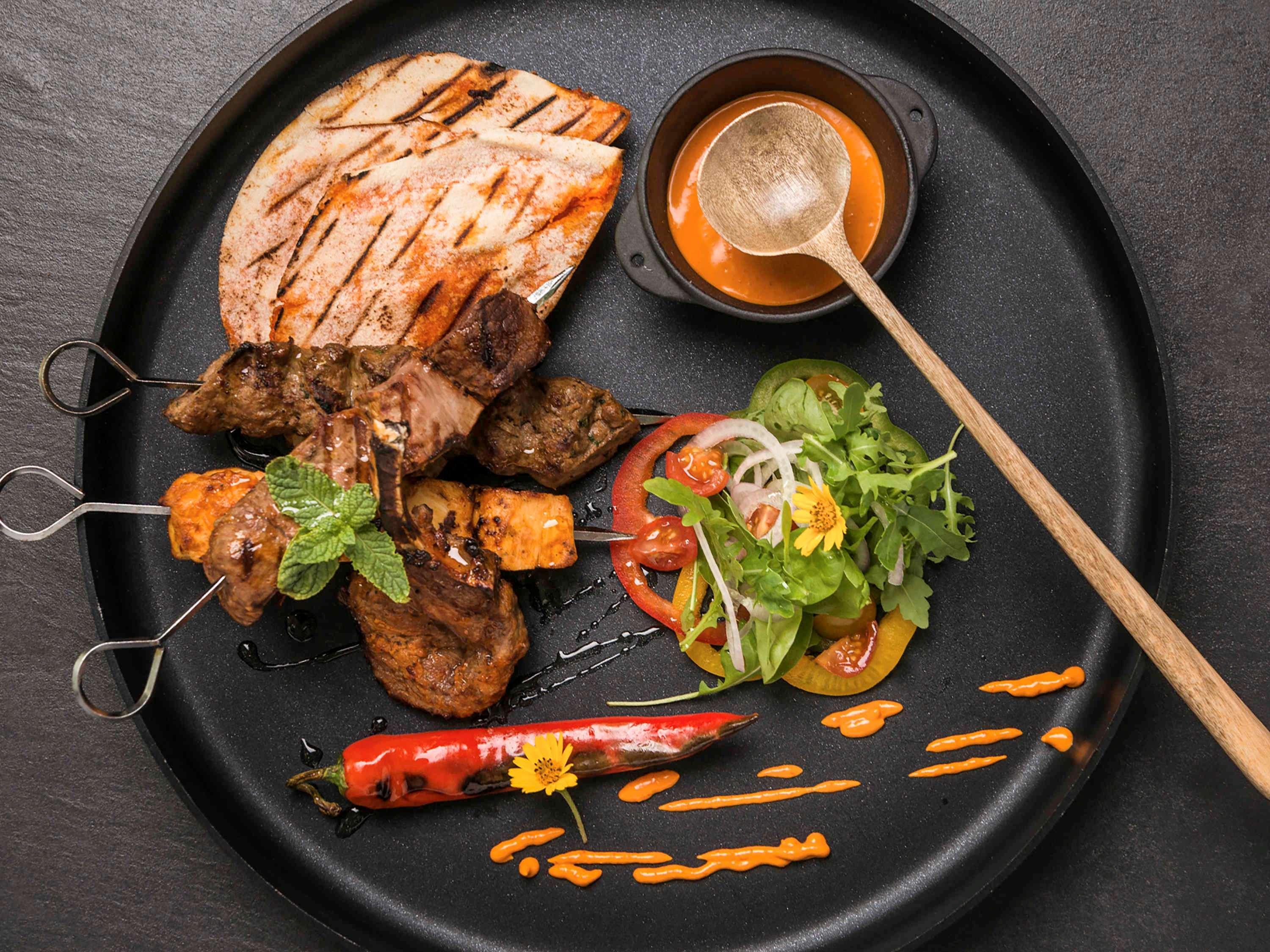 The Retreat Palm Dubai Mgallery By Sofitel Esterno foto The photo features a beautifully arranged plate of food. It includes grilled meat skewers, likely made from various types of meat, alongside a slice of grilled bread. There is also a serving of mixed salad with fresh vegetables such as tomatoes and g