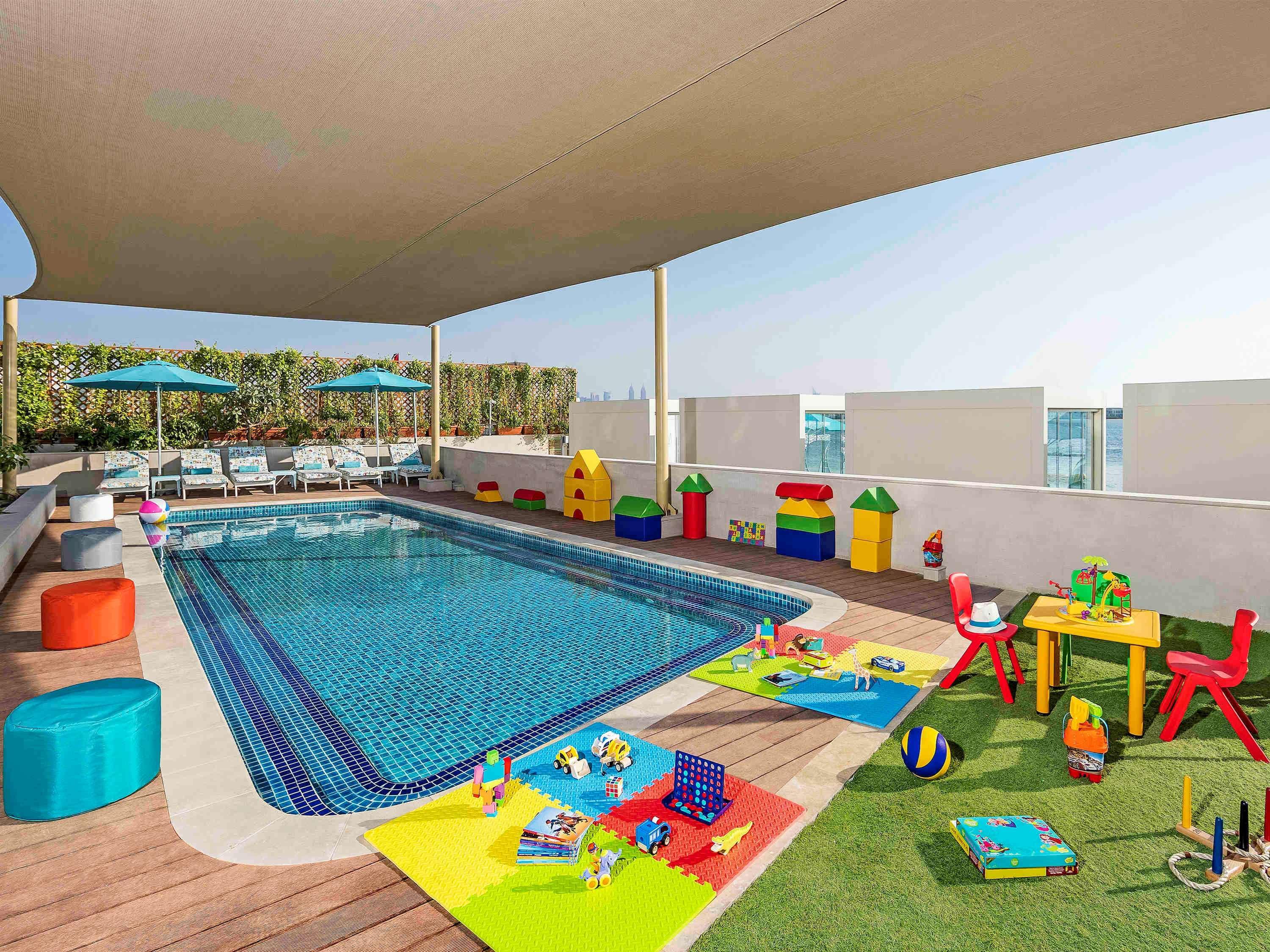 The Retreat Palm Dubai Mgallery By Sofitel Esterno foto The photo shows a bright and inviting outdoor area designed for children. It features a swimming pool with a clear, blue surface, surrounded by lounge chairs and shaded areas under umbrellas. Nearby, there are colorful play structures, including bloc