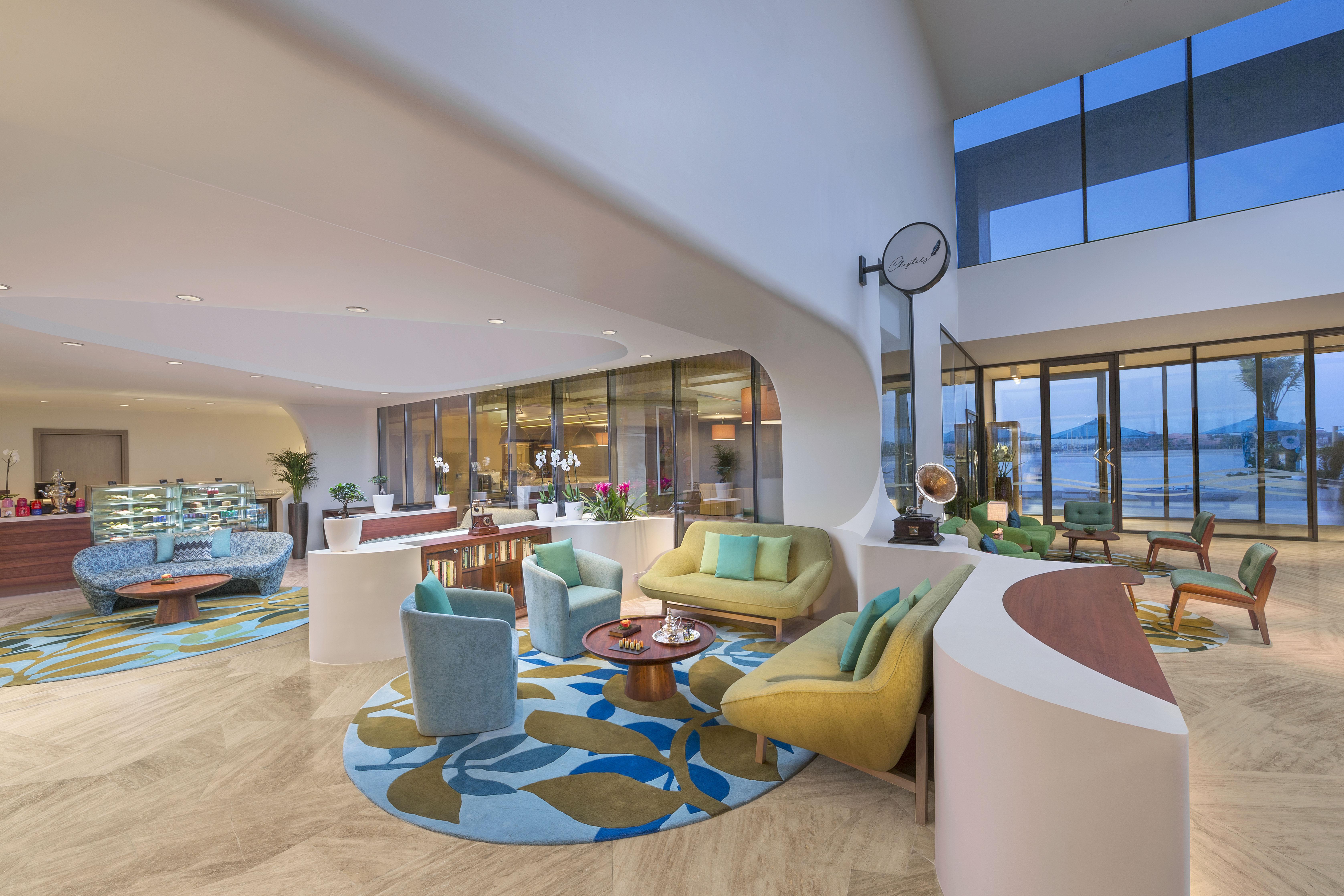 The Retreat Palm Dubai Mgallery By Sofitel Esterno foto The photo depicts a modern and stylish interior space, likely a lobby or lounge area. It features a variety of seating arrangements, including colorful chairs and a couch, all arranged around a central coffee table. The floor is adorned with a large,