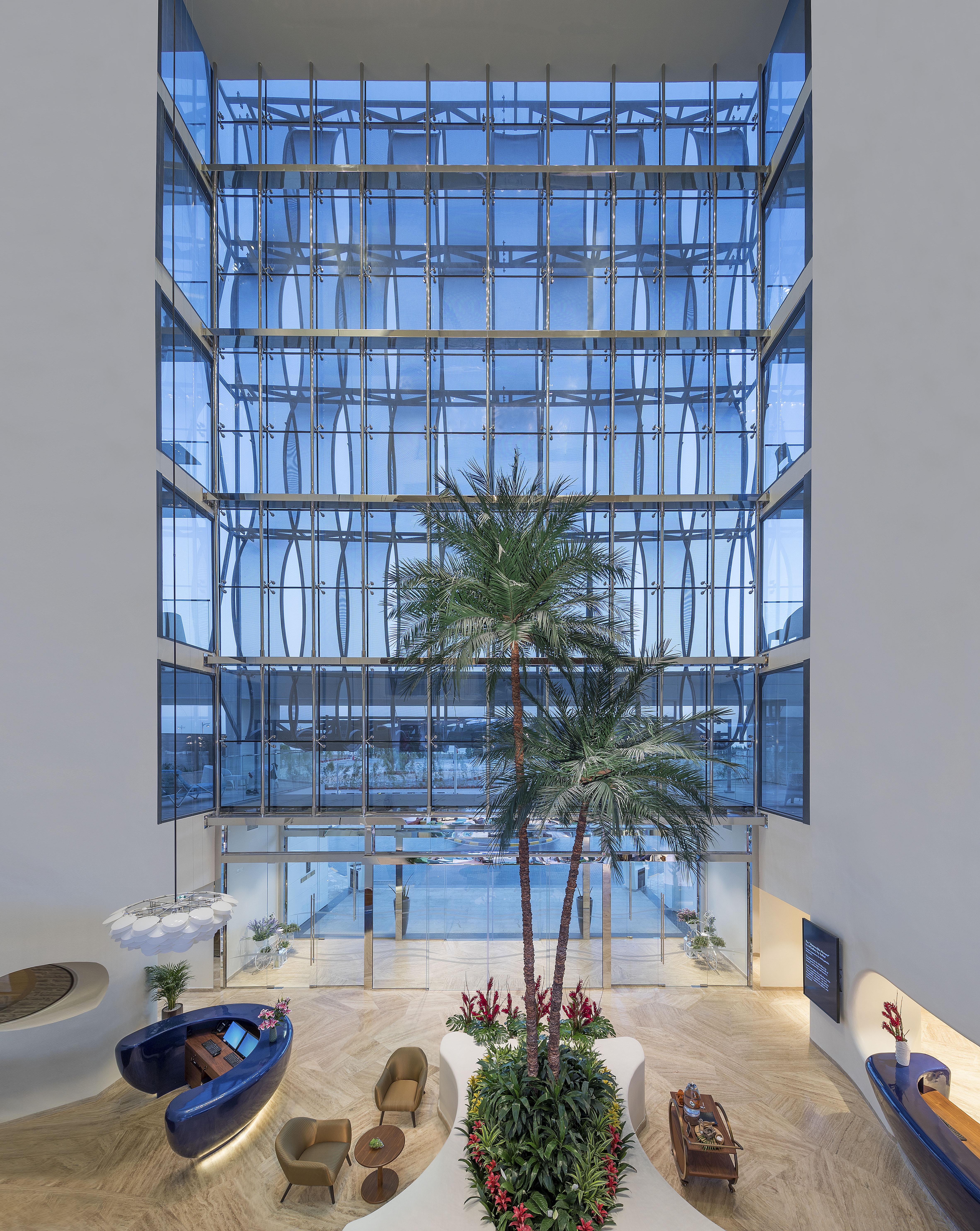 The Retreat Palm Dubai Mgallery By Sofitel Esterno foto The photo depicts a spacious and modern interior space characterized by a large glass facade that allows natural light to flood in. In the center, there are tall, lush palm trees that add a touch of greenery to the environment. The design features cl