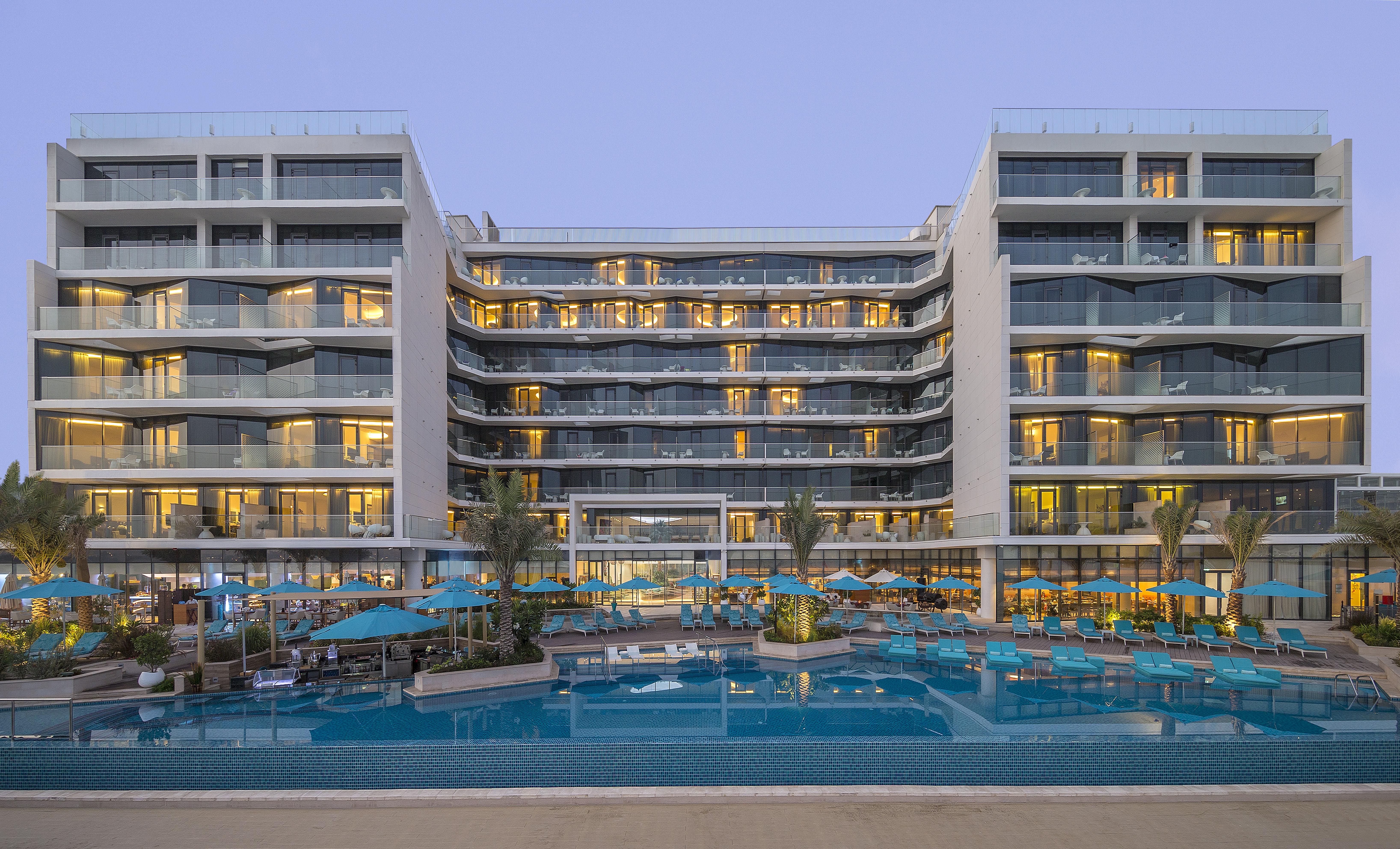 The Retreat Palm Dubai Mgallery By Sofitel Esterno foto The photo shows a modern hotel or resort with a stylish architectural design. The building features multiple stories, large glass windows, and balconies that give it a contemporary look. In front of the hotel, there is a swimming pool surrounded by l