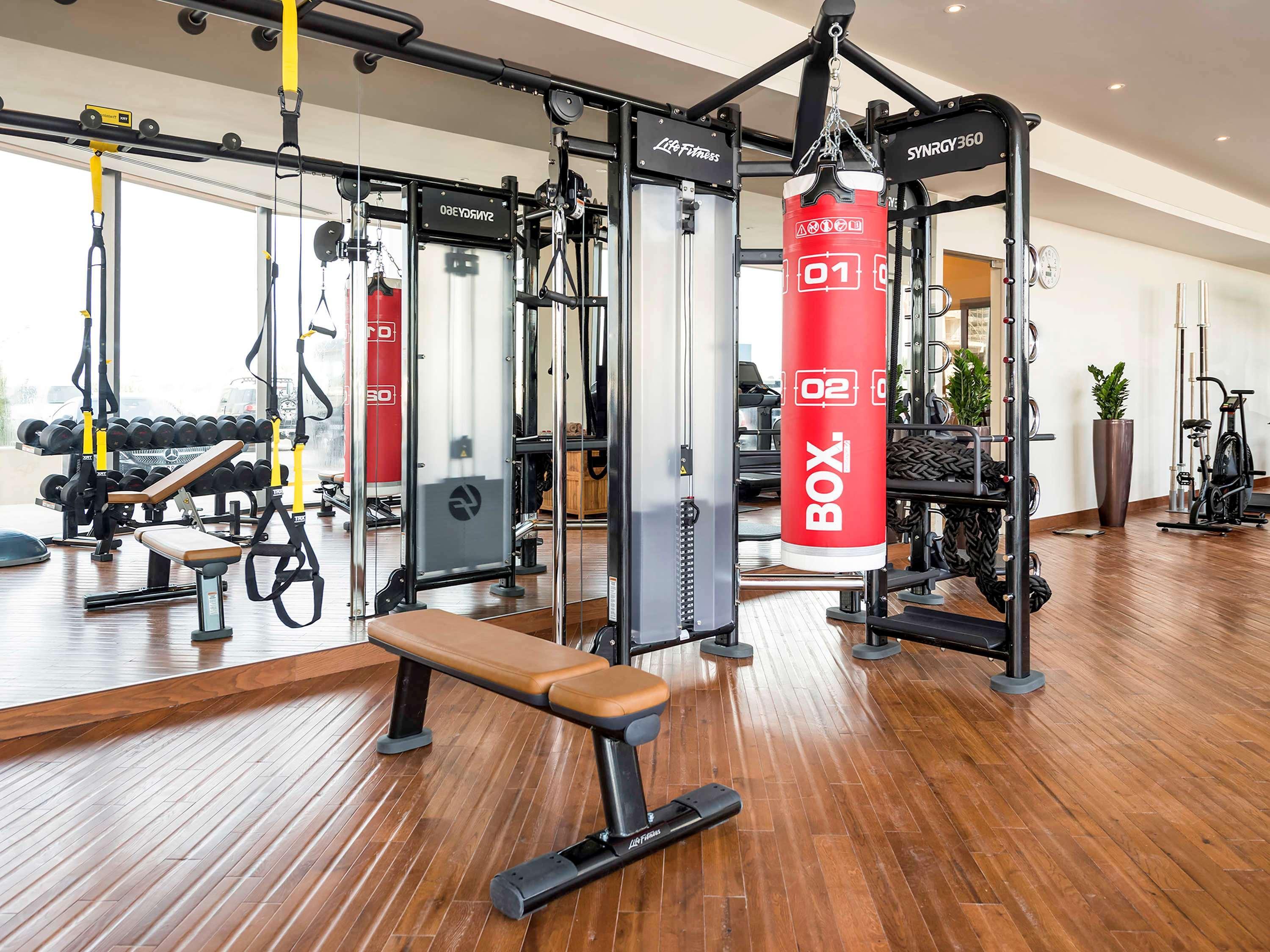 The Retreat Palm Dubai Mgallery By Sofitel Esterno foto The photo shows a modern gym interior. It features various workout equipment, including a cable machine with multiple pulley systems for resistance training. There is a bright red punching bag labeled "BOX," and a wooden bench for workouts. The floor