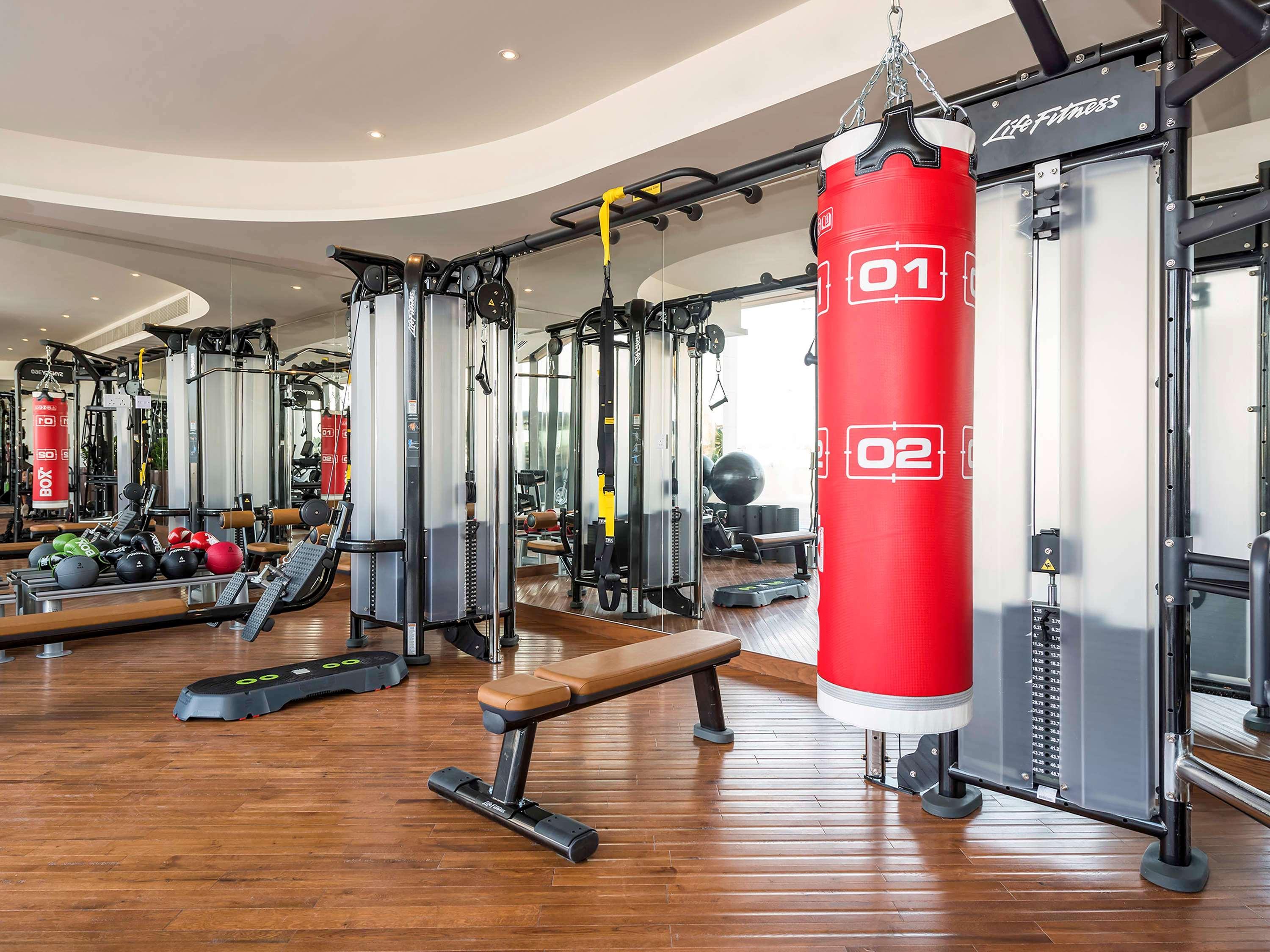 The Retreat Palm Dubai Mgallery By Sofitel Esterno foto The photo depicts an interior of a gym or fitness center. It features a variety of exercise equipment, including:

- A red punching bag hanging from the ceiling, marked with numbers "01" and "02."
- Several multi-use cable machines for strength train
