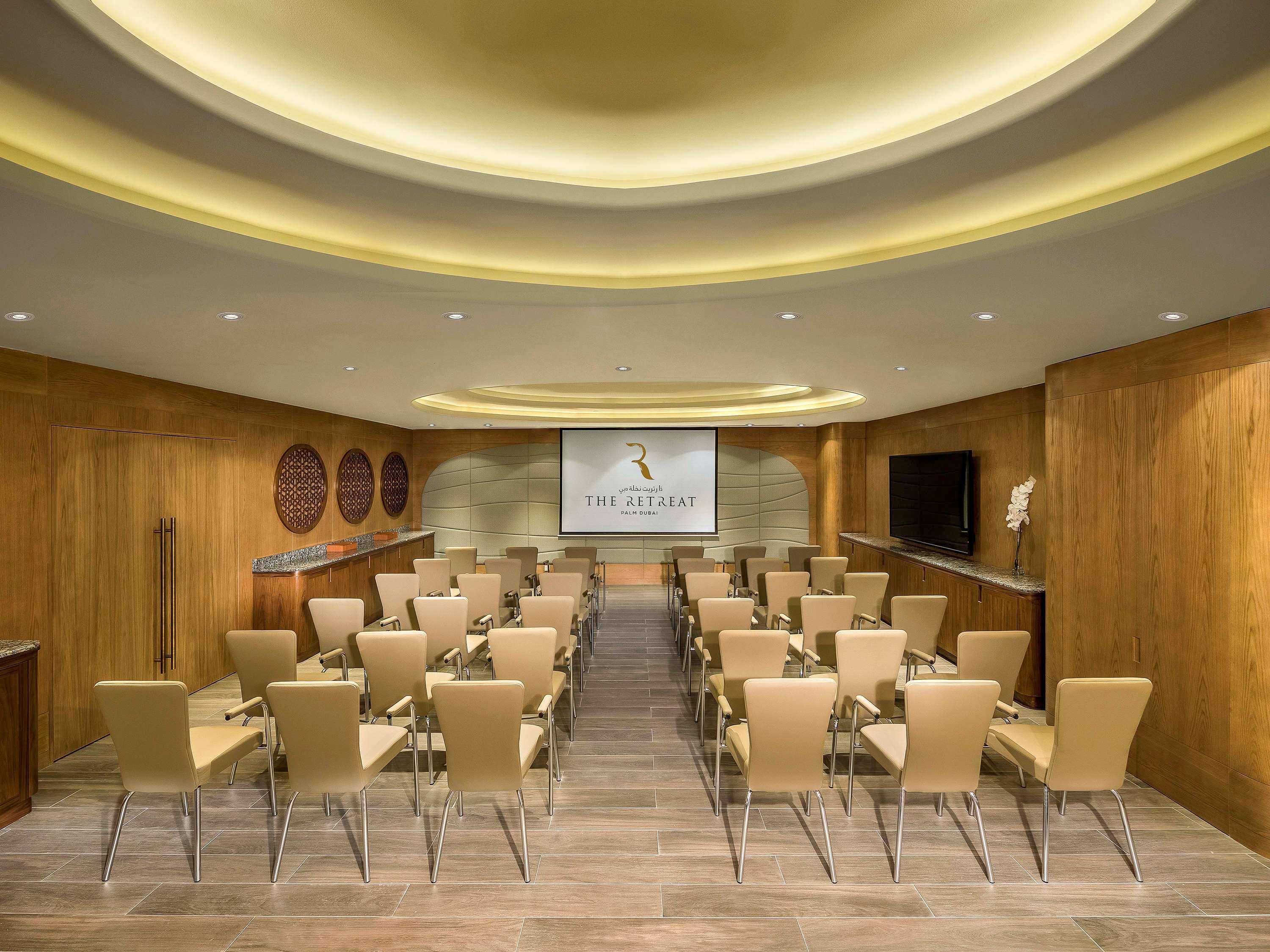 The Retreat Palm Dubai Mgallery By Sofitel Esterno foto The photo shows a modern conference or meeting room designed for presentations or gatherings. It features rows of beige chairs arranged facing a screen at the front of the room, which displays the name "The Ritz" or a similar logo. The walls are made