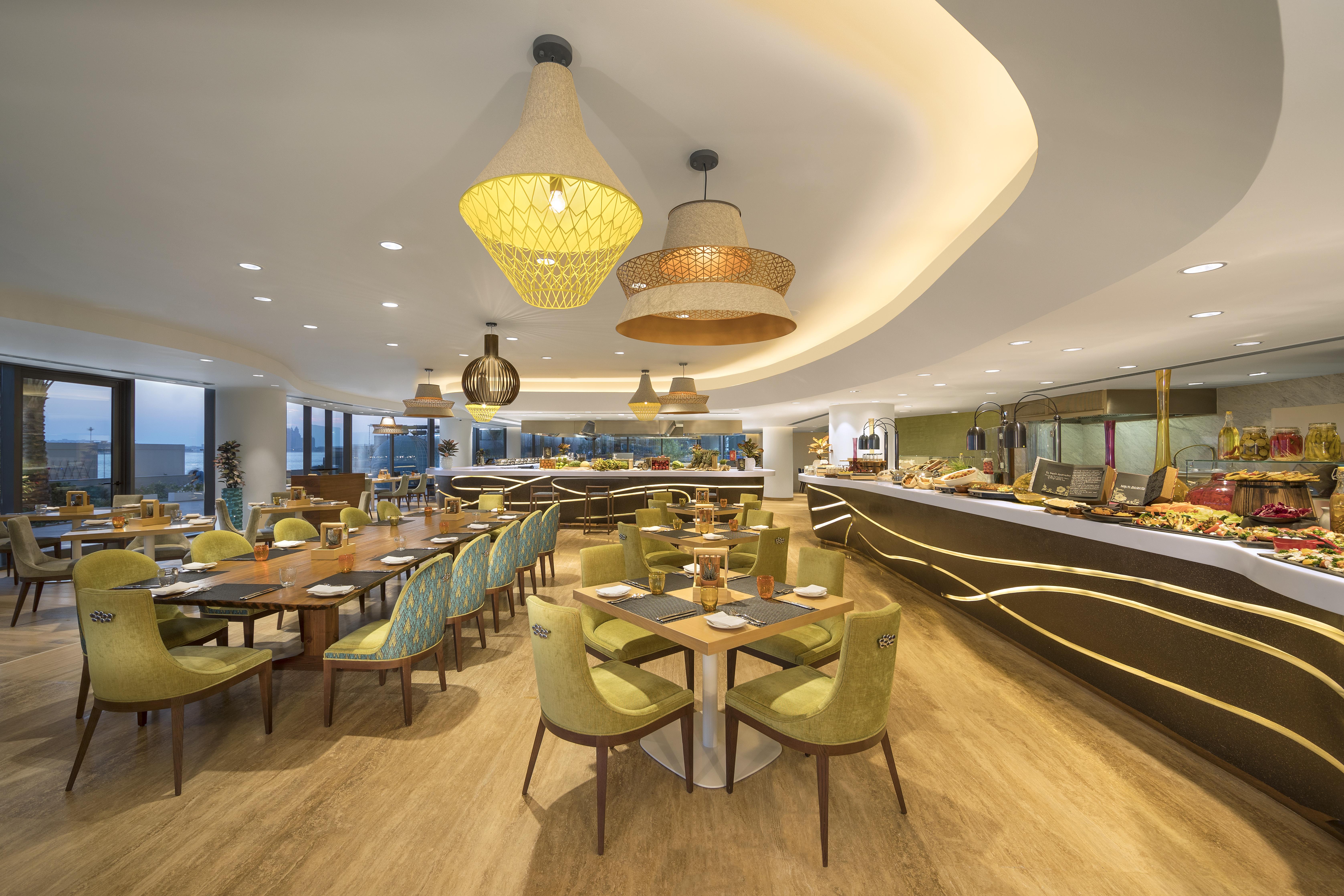 The Retreat Palm Dubai Mgallery By Sofitel Esterno foto The photo shows a modern restaurant interior. It features a spacious dining area with wooden floors and a variety of tables and chairs. The chairs are predominantly green, and the tables are arranged to accommodate groups. The ceiling is adorned with