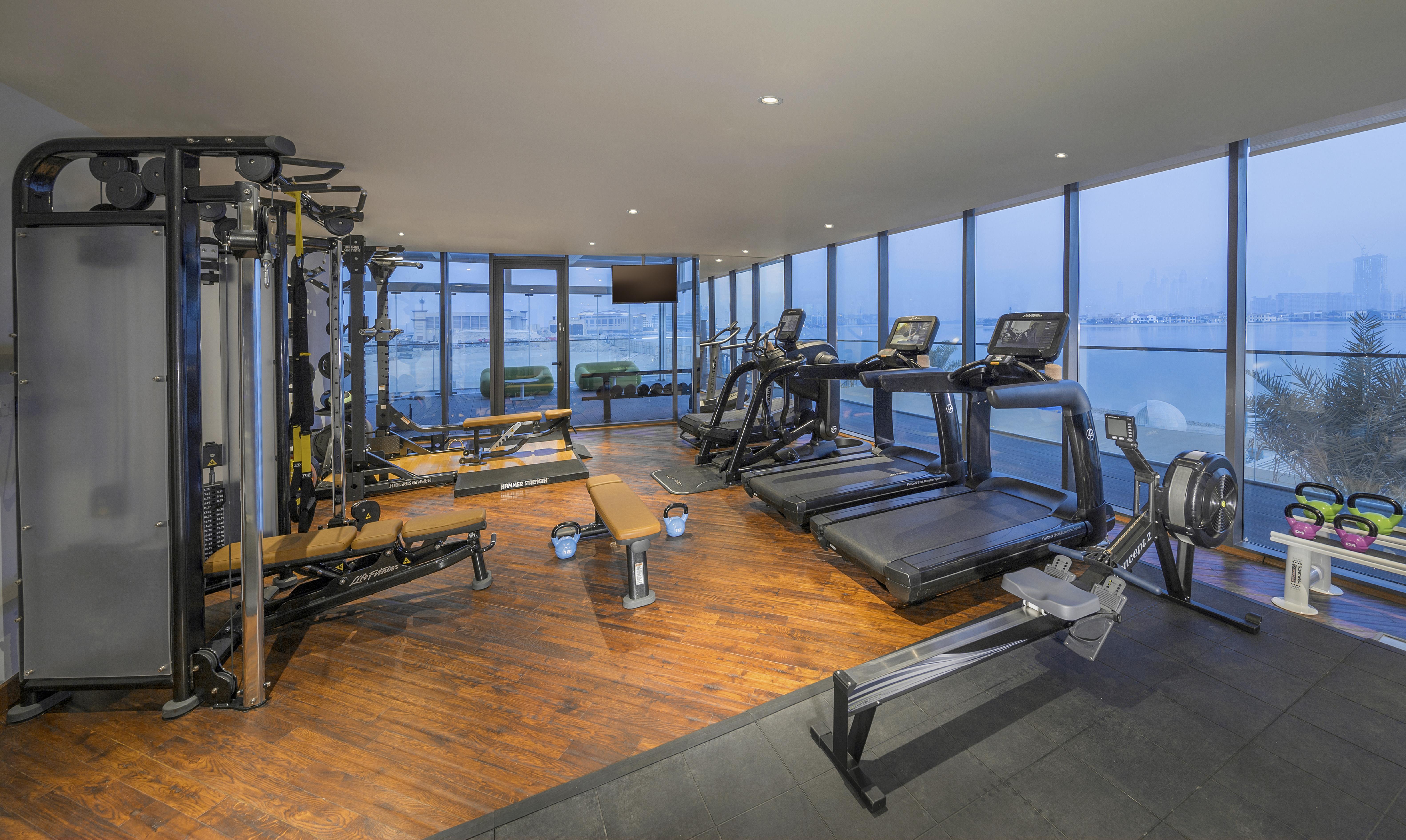 The Retreat Palm Dubai Mgallery By Sofitel Esterno foto The photo shows a modern gym or fitness area with large windows offering a view outside. It features various workout equipment, including:

- Treadmills positioned against the windows
- Rowing machines
- Strength training machines
- Workout benches

