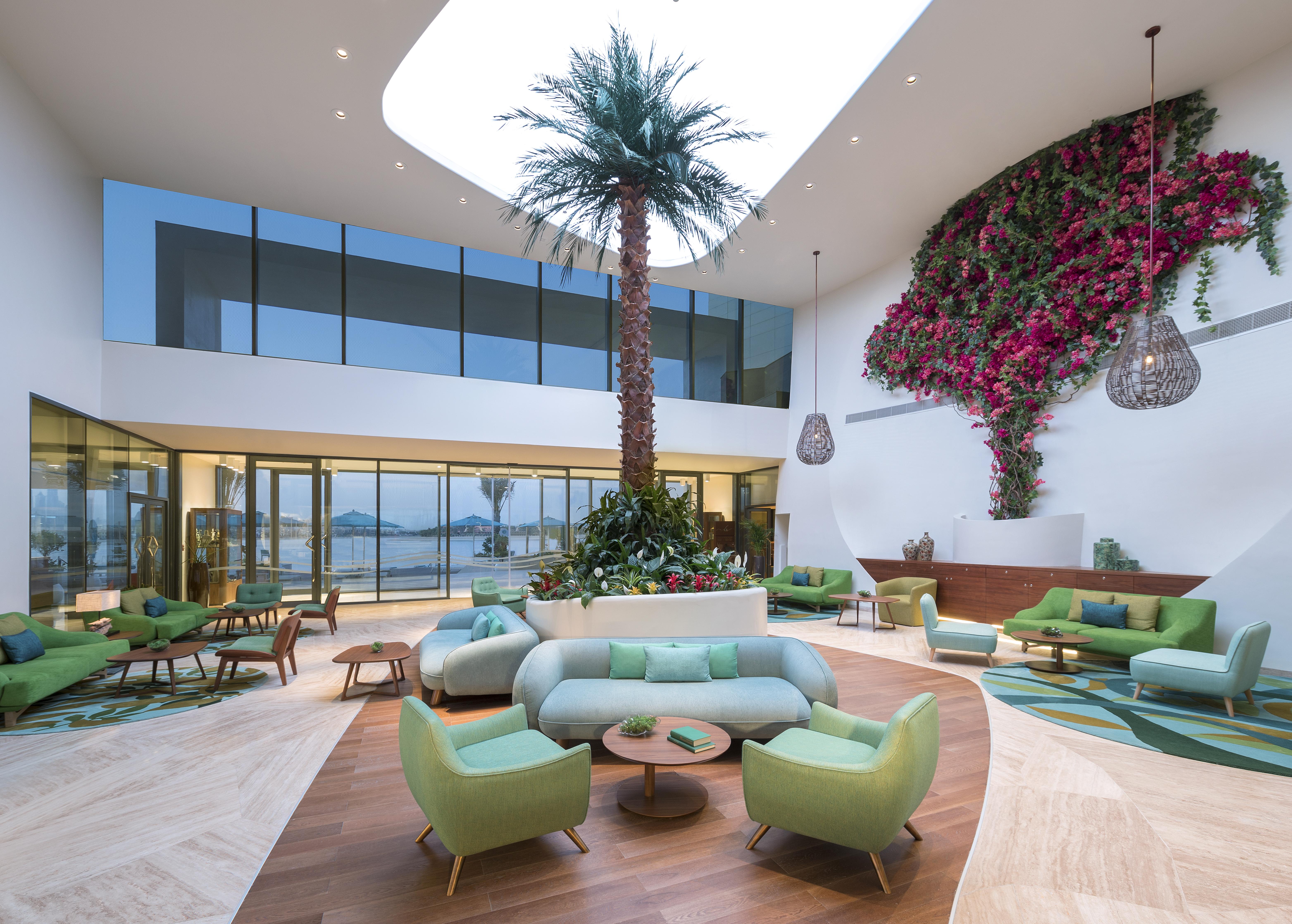 The Retreat Palm Dubai Mgallery By Sofitel Esterno foto The photo depicts a modern and stylish interior space that features lush green seating arrangements in various shades. A large palm tree serves as a focal point, reaching toward a skylight that allows natural light to flood the area. The walls are ad