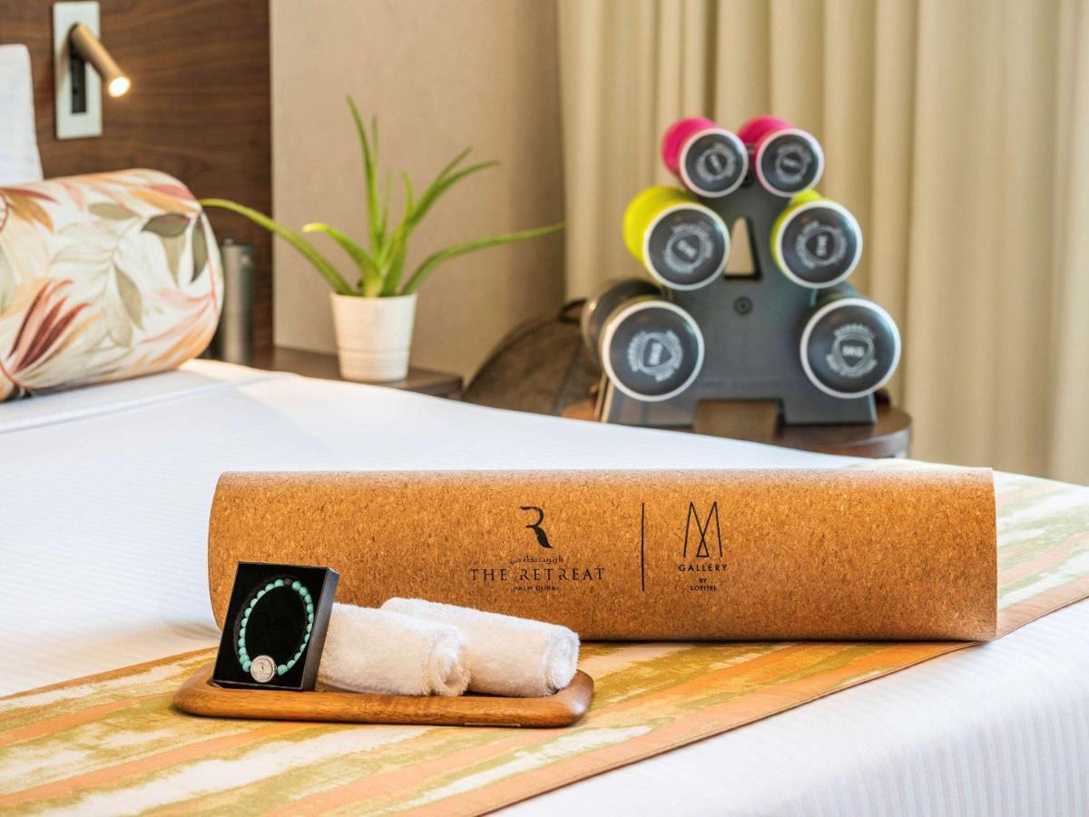 The Retreat Palm Dubai Mgallery By Sofitel Esterno foto The photo shows a well-decorated hotel room with a neatly made bed. On the bed, there is a cylindrical cork container with a logo, indicating a brand or establishment. Next to it, there are two rolled-up towels resting on a small wooden tray. In the 