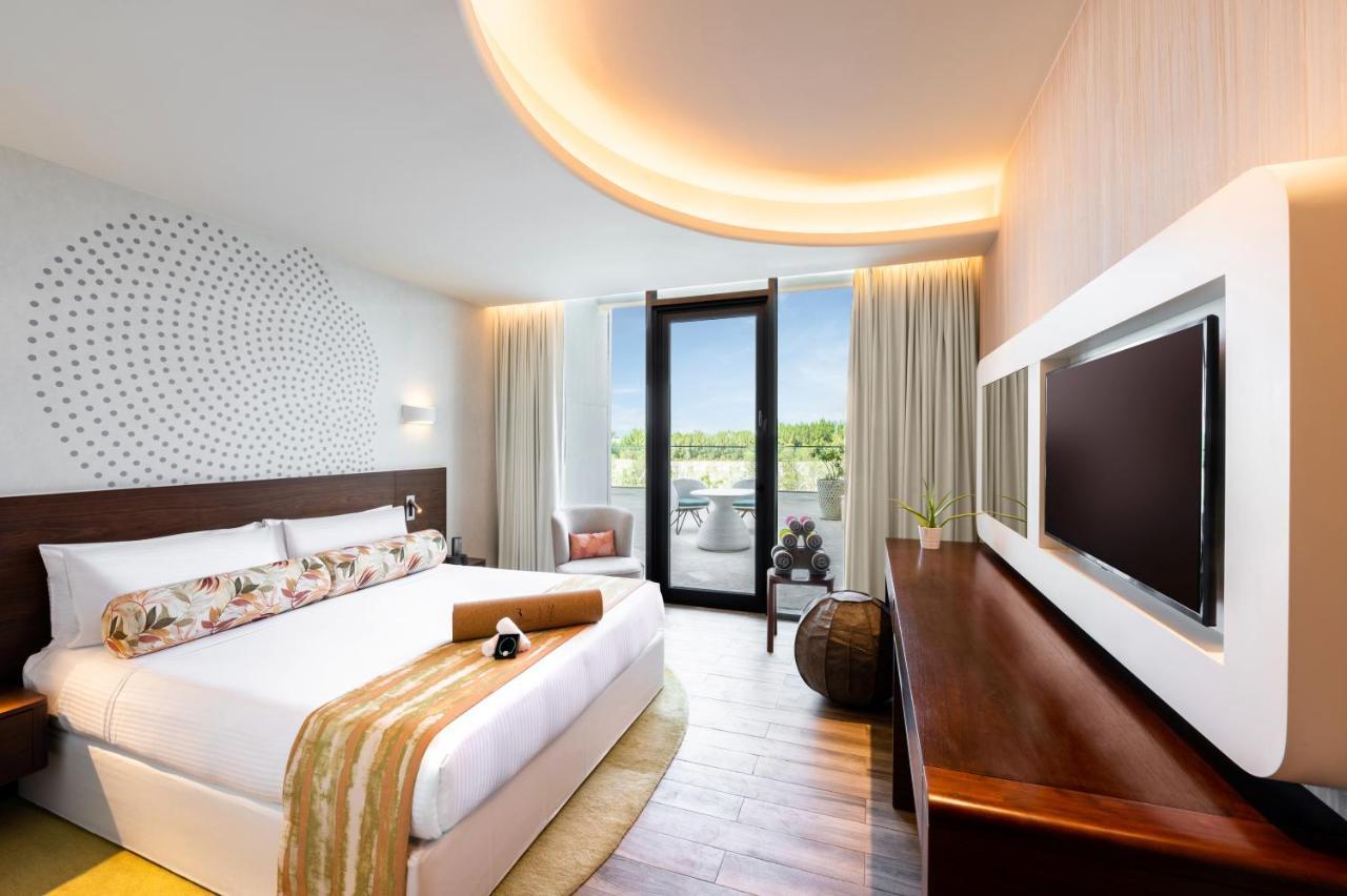 The Retreat Palm Dubai Mgallery By Sofitel Esterno foto The image shows a stylish hotel room with a modern design. It features a spacious king-size bed with a decorative throw and pillow. The wall behind the bed has a unique pattern, adding a contemporary touch. There is a large window that allows natural