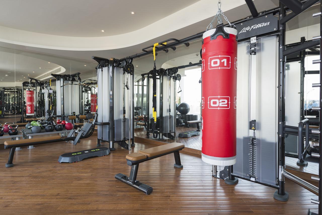 The Retreat Palm Dubai Mgallery By Sofitel Esterno foto The photo shows a well-equipped gym interior. It features a red punching bag hanging from a ceiling mount, surrounded by various fitness equipment. On one side, there are multiple cable machines for strength training, and in front of them is a wooden