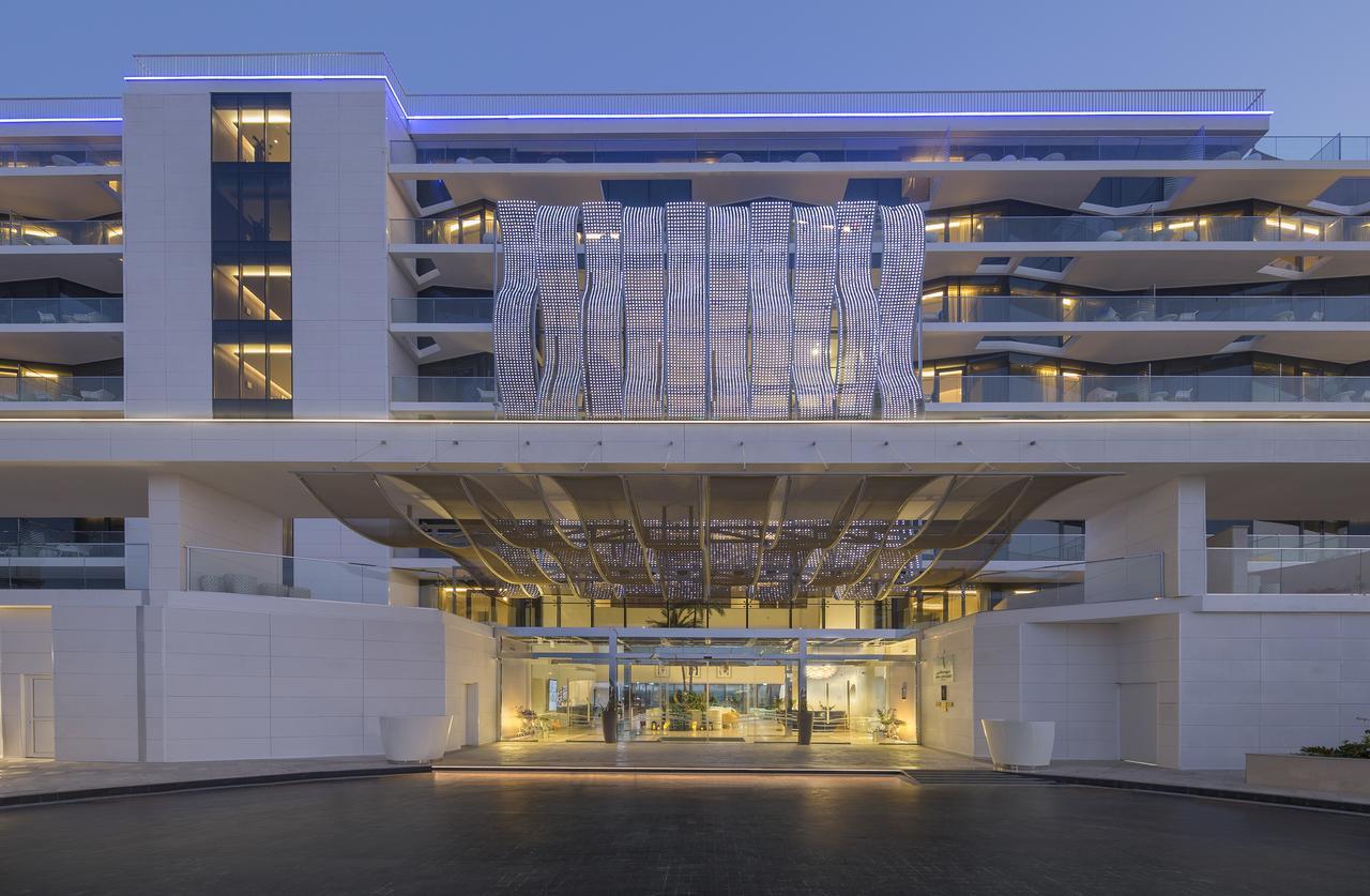 The Retreat Palm Dubai Mgallery By Sofitel Esterno foto The photo shows a modern building with a sleek architectural design. It features multiple stories and a striking entrance that has a unique, artistic canopy overhead. The exterior is primarily white, highlighting clean lines and a contemporary aesthe