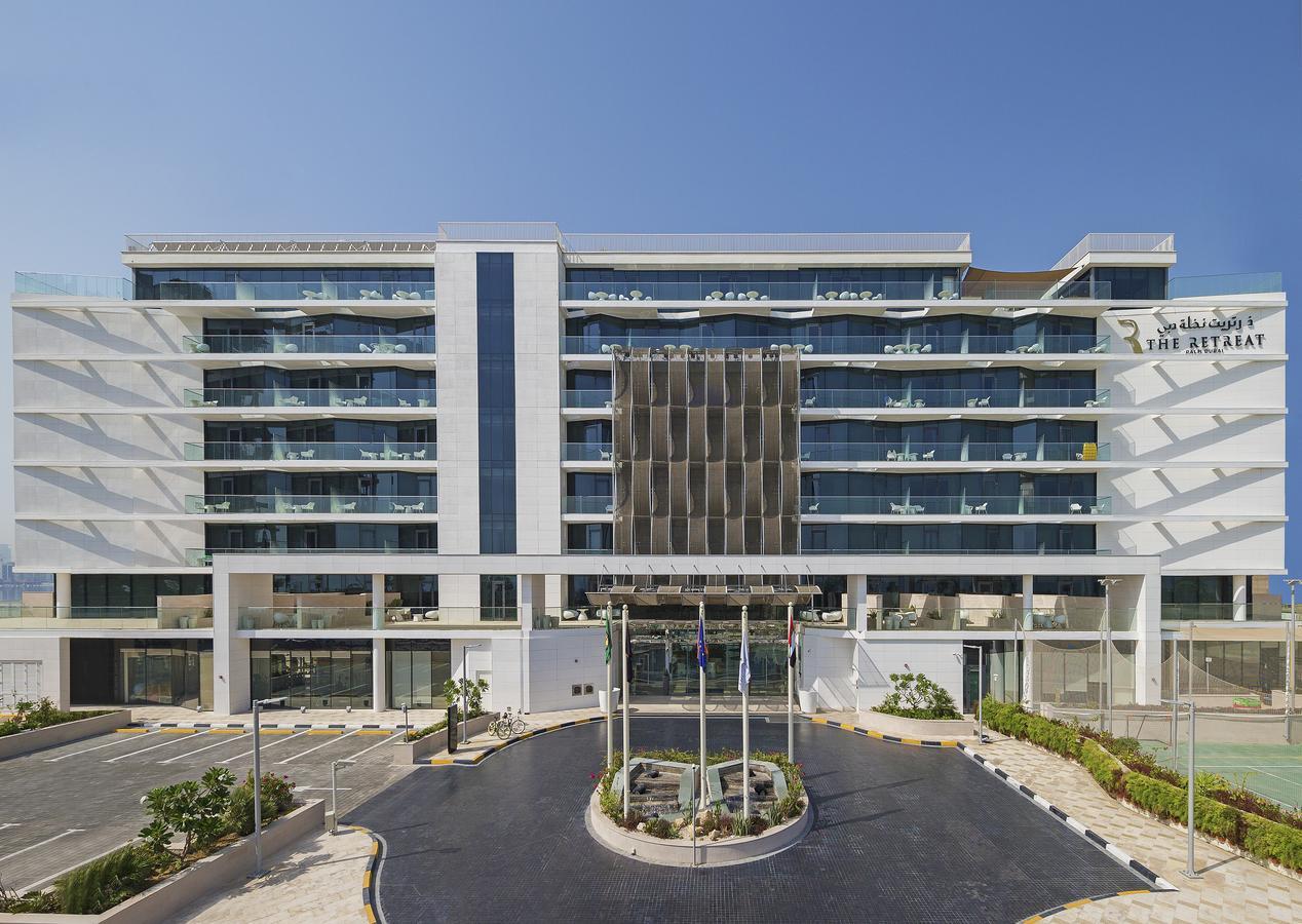 The Retreat Palm Dubai Mgallery By Sofitel Esterno foto The photo shows a modern hotel building with an exterior characterized by a sleek design. The structure features multiple stories with balconies, a combination of large glass windows, and a clean, white facade. In front of the hotel, there is a lands