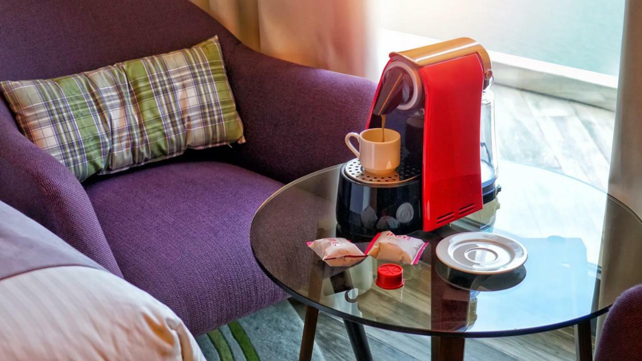 The Retreat Palm Dubai Mgallery By Sofitel Esterno foto The photo shows a cozy setting featuring a purple armchair with a plaid cushion. In front of the chair, there is a round glass table that holds a red coffee machine, which is dispensing coffee into a white cup. Next to the coffee machine, there are t
