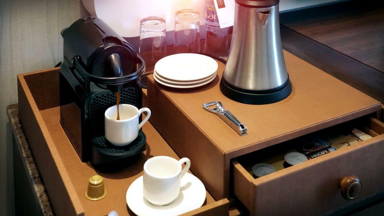 The Retreat Palm Dubai Mgallery By Sofitel Esterno foto The photo shows a coffee station set up on a wooden surface. It features a Nespresso coffee machine with a coffee cup placed on it, filled with brewed coffee. Beside the coffee machine, there are several white plates stacked and a sleek metallic kett